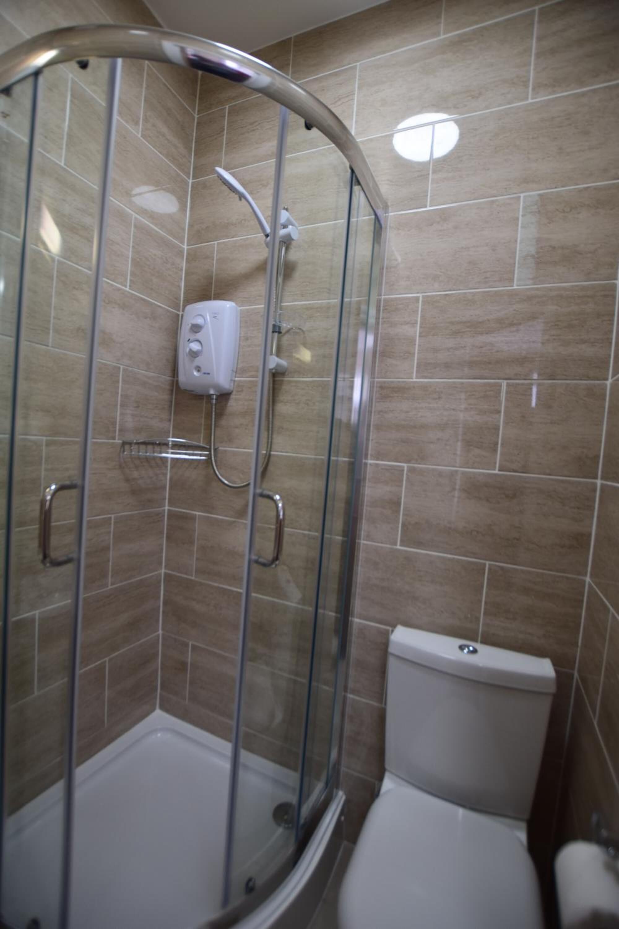 A shower enclosure with a glass door, a handheld showerhead, and a control panel.