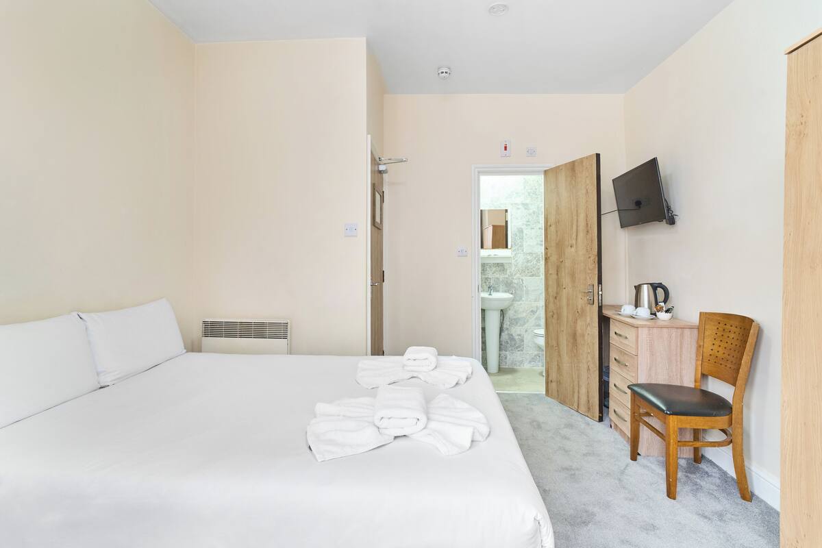 A hotel room with a bed, a wooden chair, a desk with a TV, and a bathroom visible through an open door.
