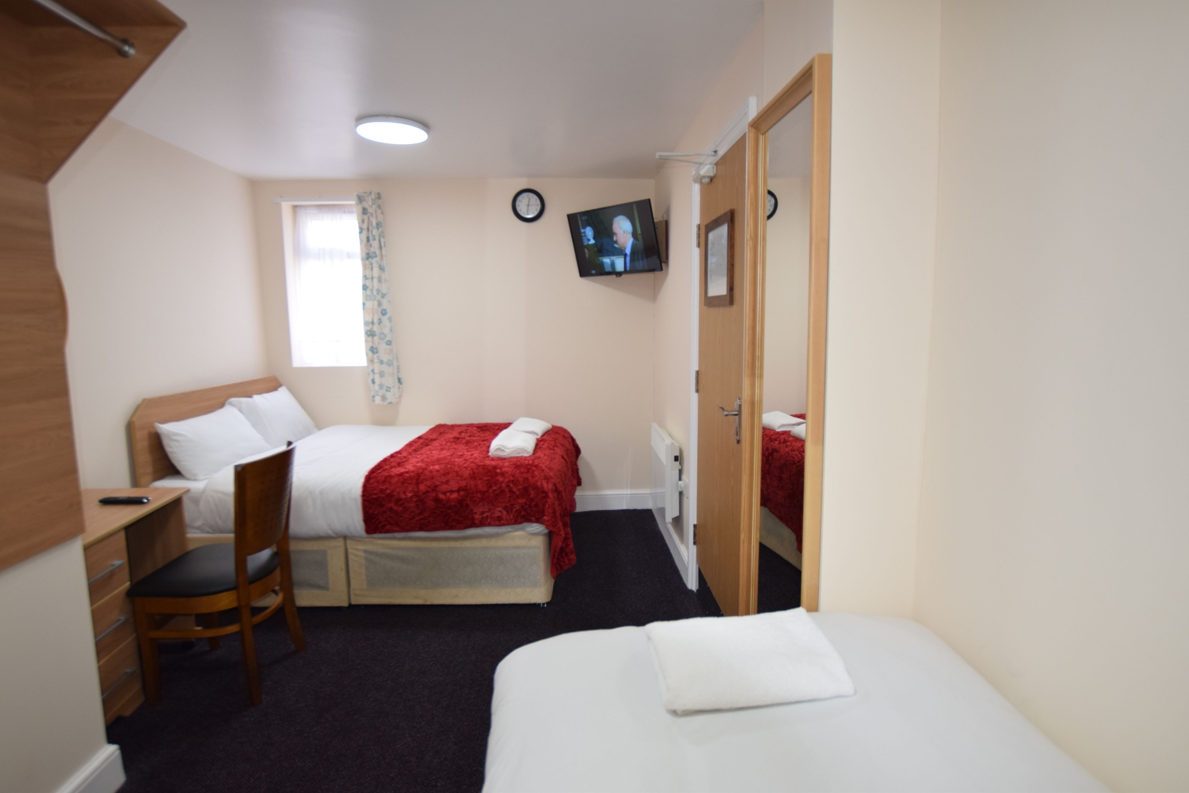 A hotel room with two beds, a desk, a chair, a television, and a window with curtains.