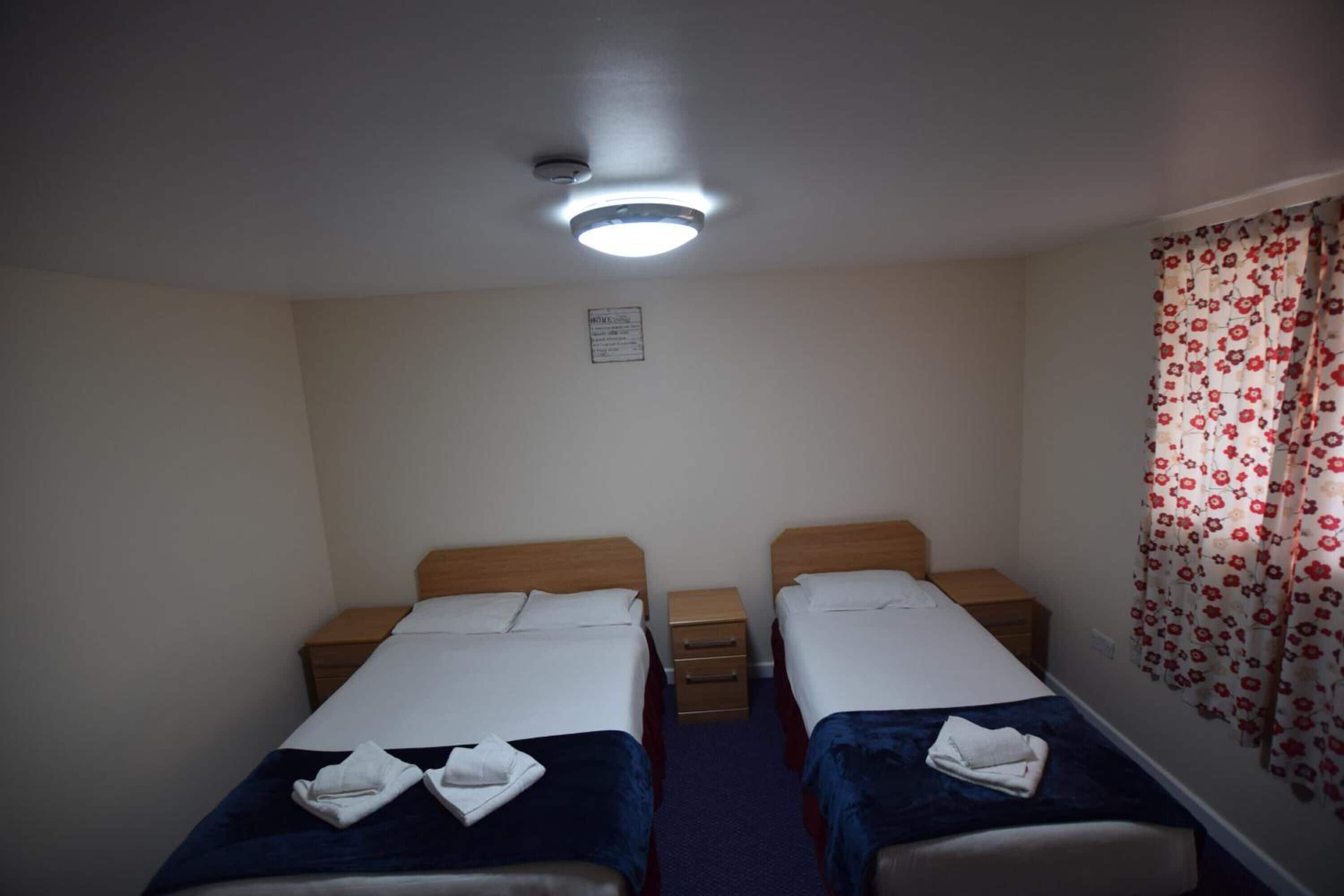 Une chambre double avec deux lits simples, une petite table de chevet et une lampe de chevet, ainsi qu’un luminaire au plafond.