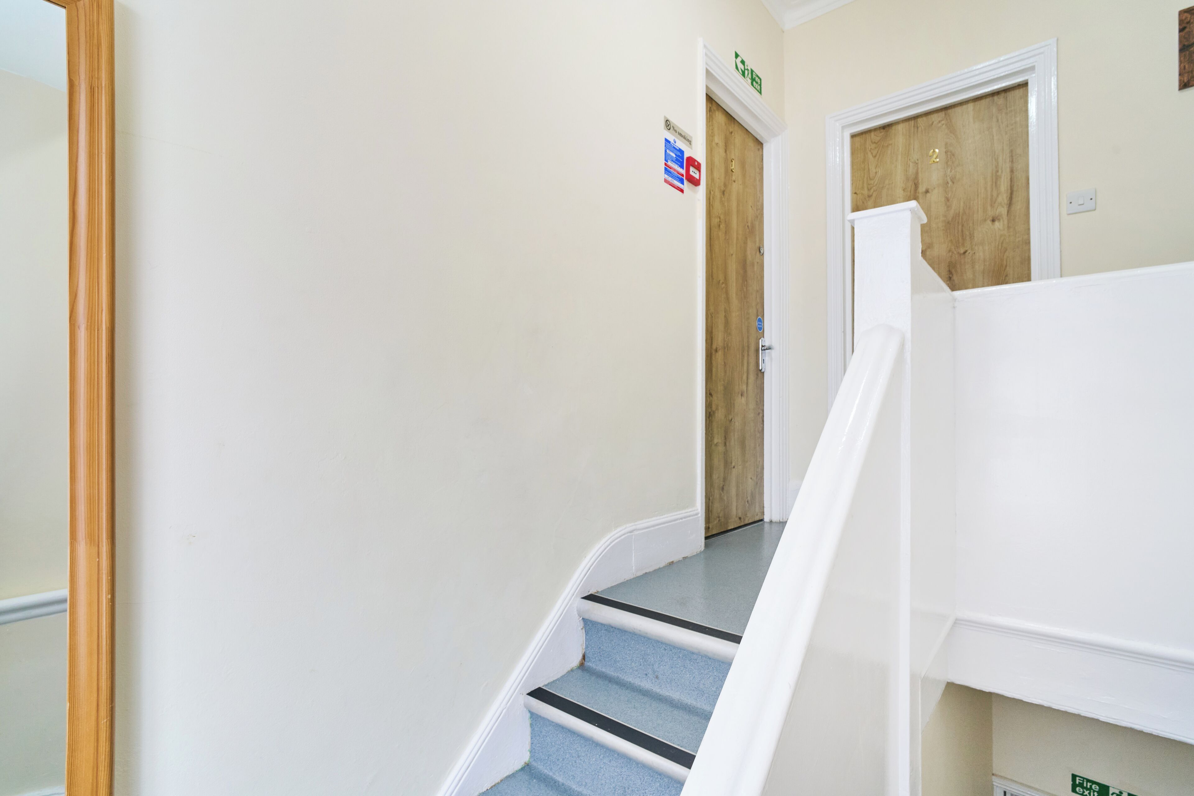 Un escalier avec des rampes blanches, une porte en bois et une enseigne fixée au mur.