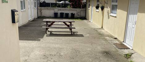A courtyard with a picnic table, a white door, and a wall-mounted trash bin.