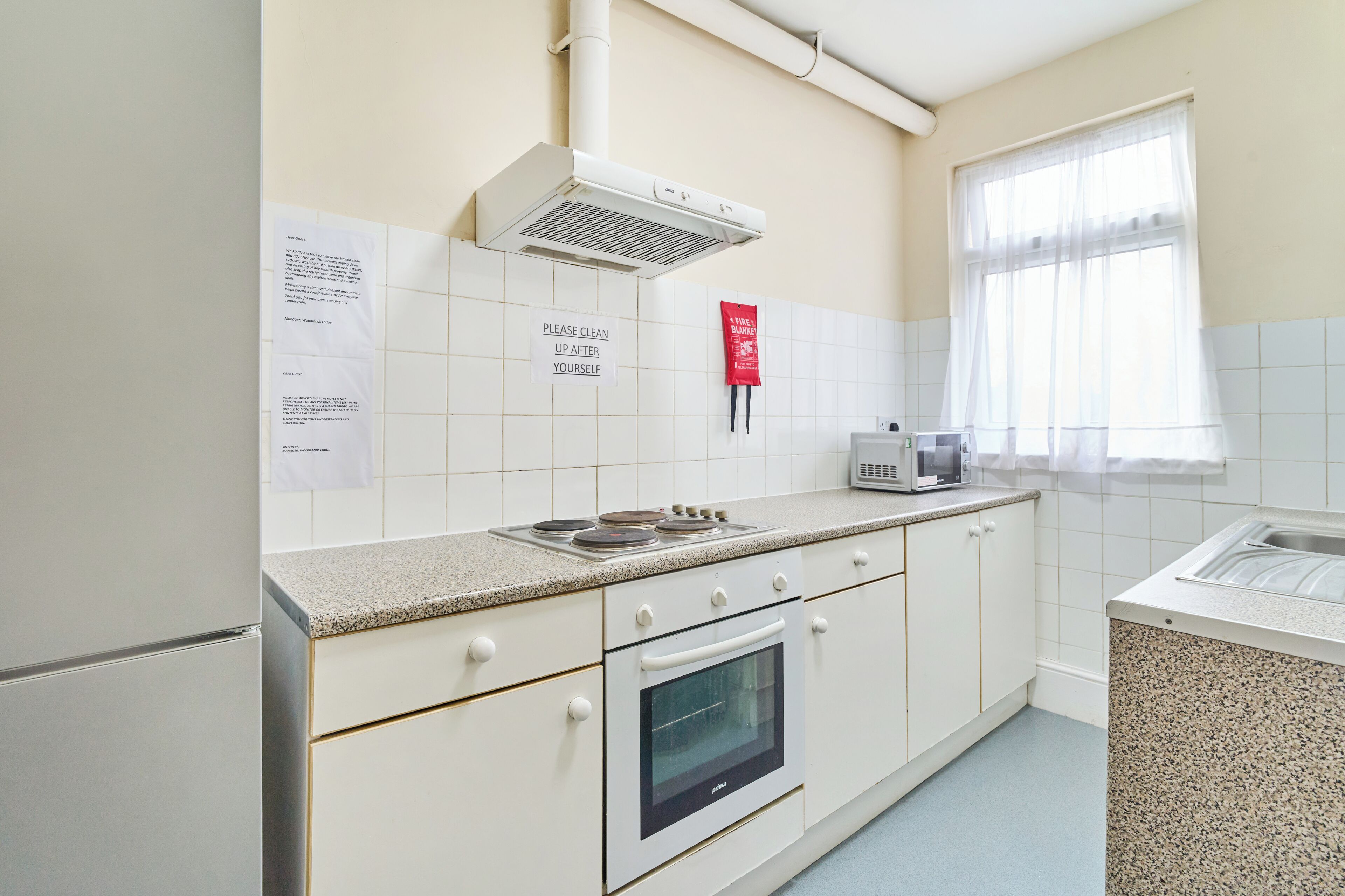 Una cocina con armarios blancos, estufa, microondas y una ventana con cortinas traslúcidas.