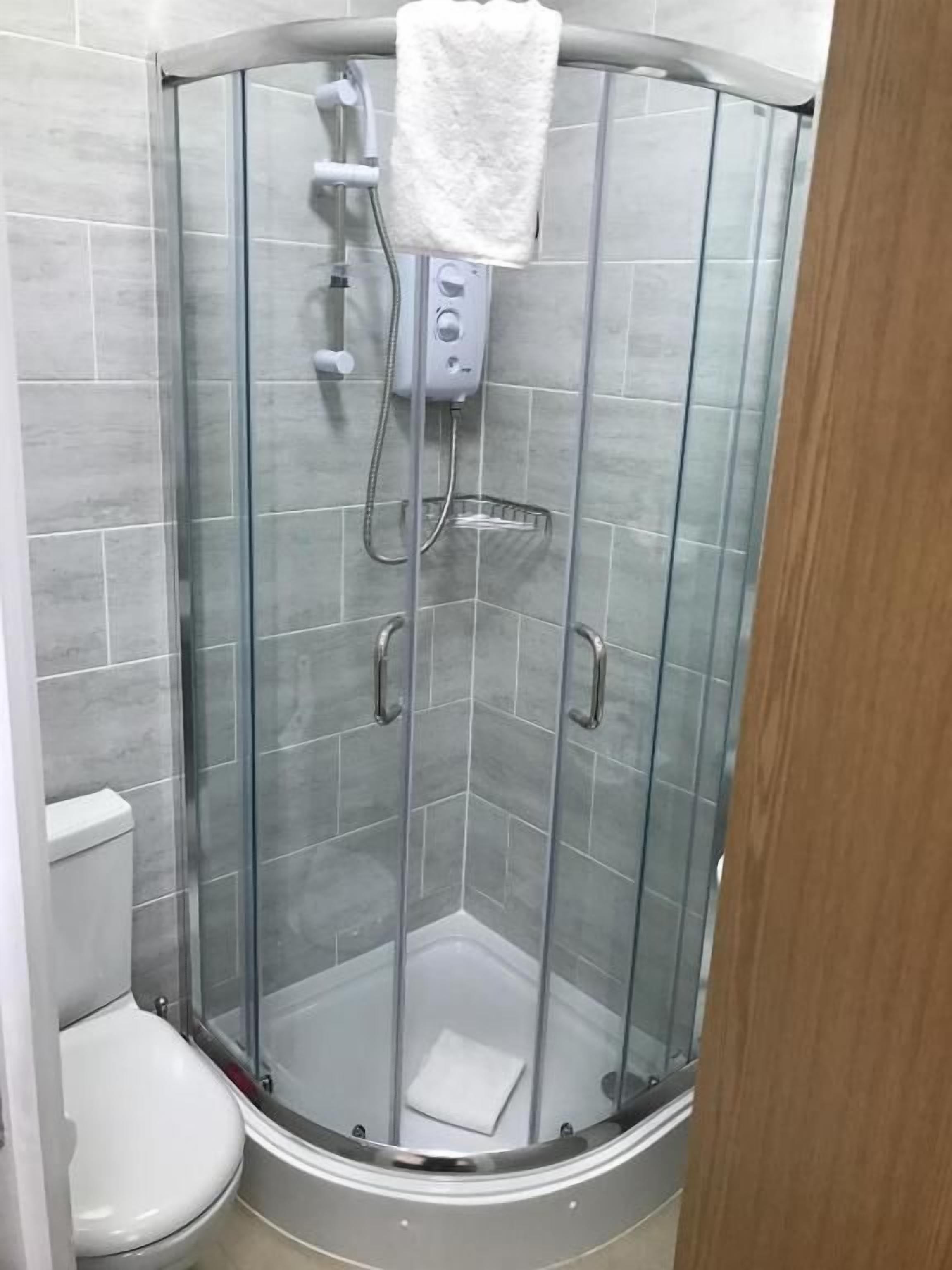 A glass-enclosed shower stall with a handheld showerhead and a towel hanging on the wall.