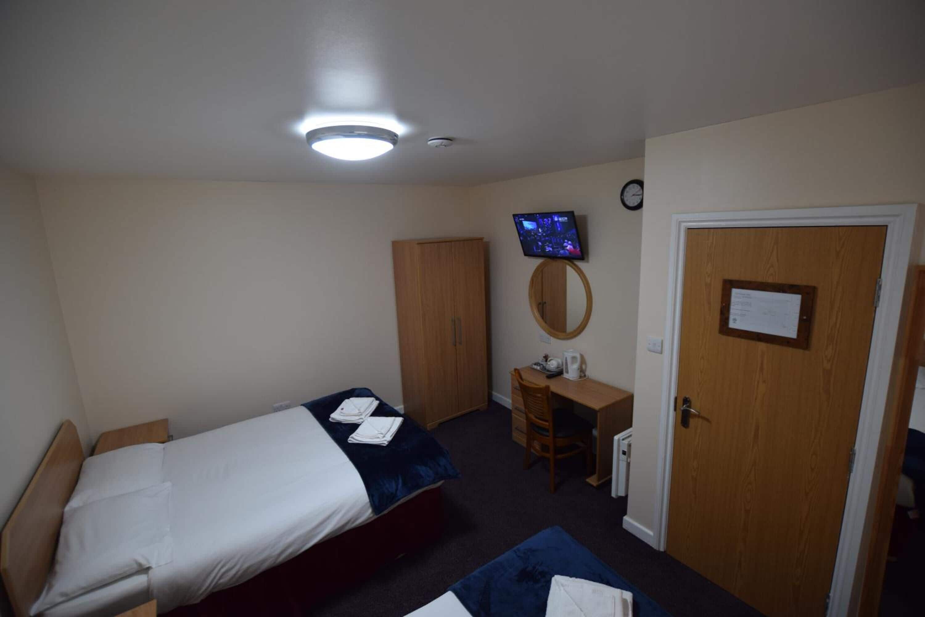 A bedroom with a bed, a desk, a chair, a wardrobe, a television, and a door with a notice.