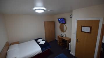 A bedroom with a bed, a desk, a chair, a wardrobe, a television, and a door with a notice.