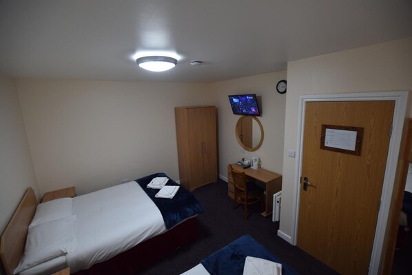 A bedroom with a bed, a desk, a chair, a wardrobe, a television, and a door with a notice. - Woodlands Lodge Ilford (Ilford)