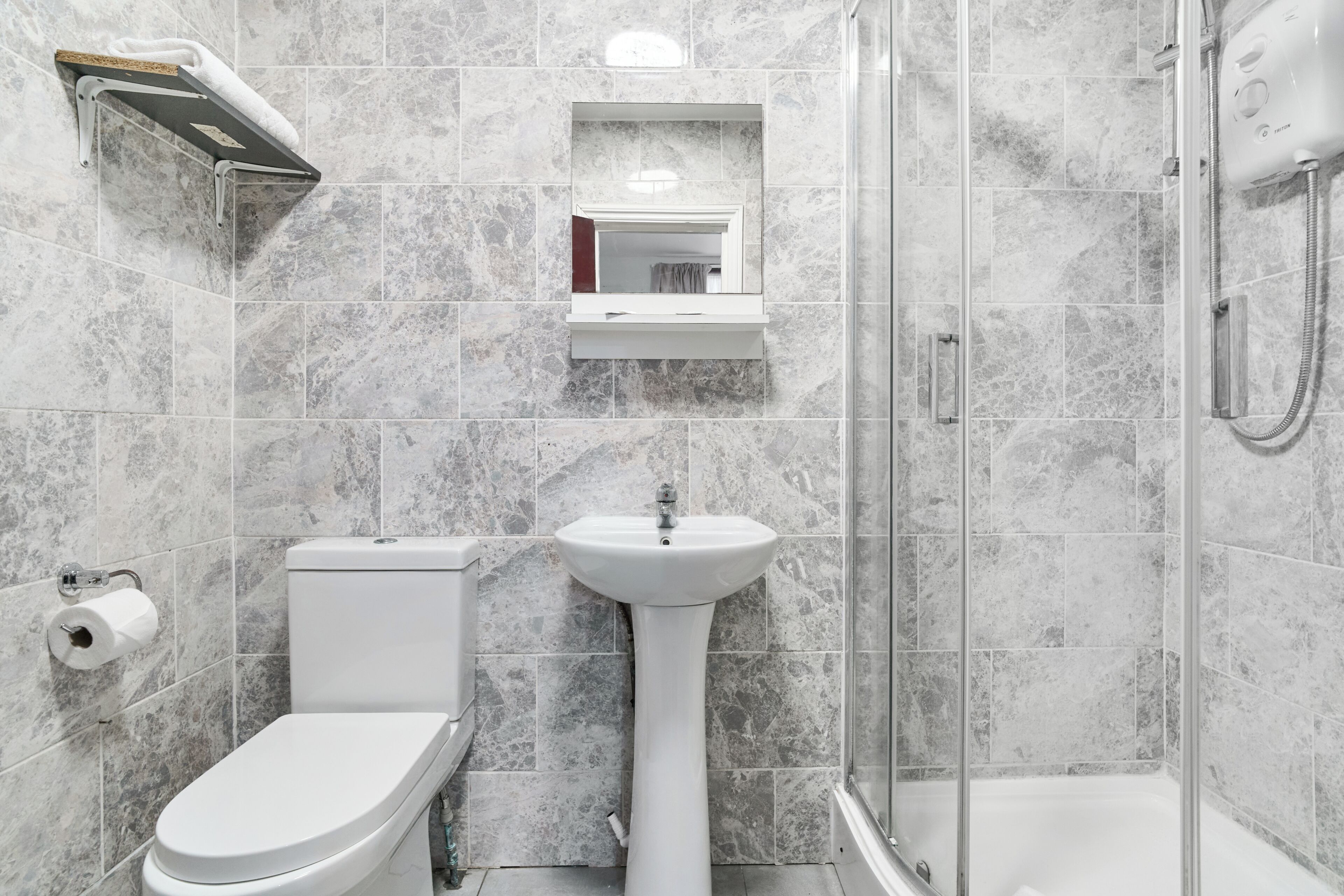 A bathroom with a toilet, sink, shower, and a mirror above the sink.