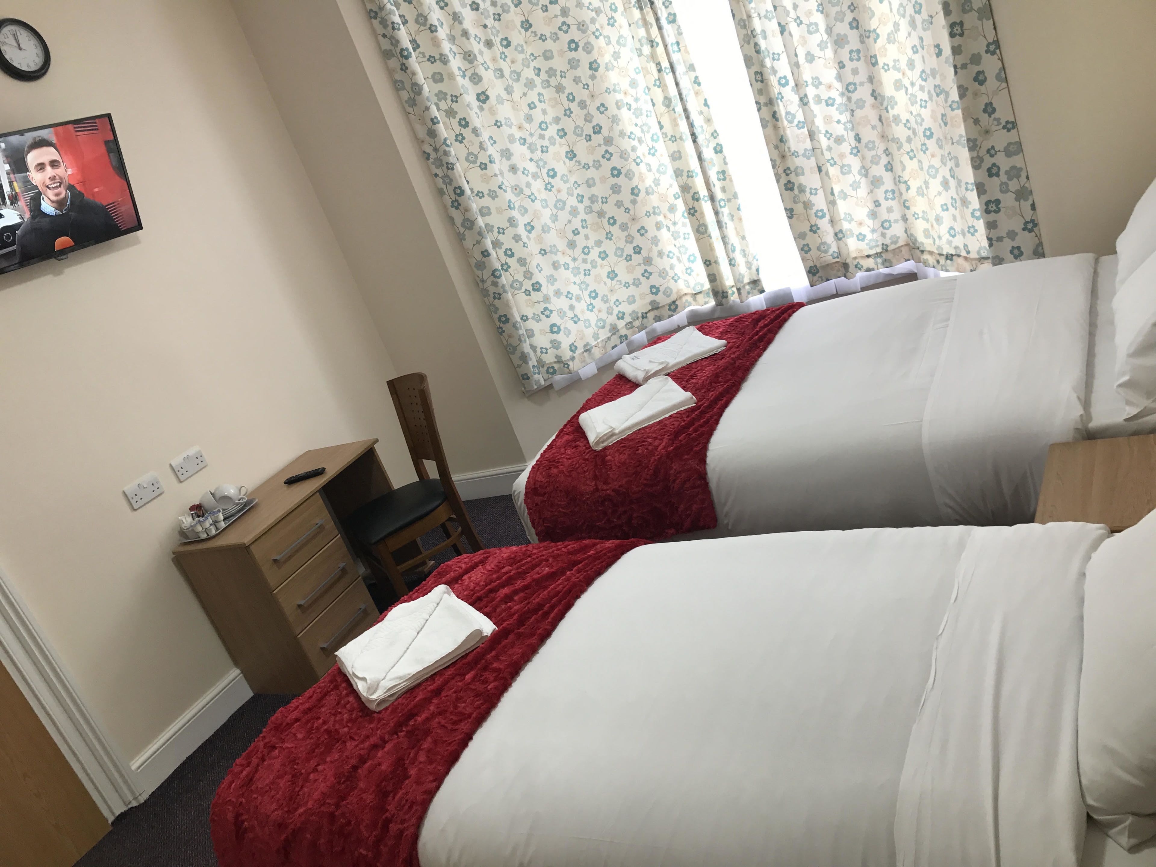 A hotel room with two beds, a wooden dresser, a desk, and a television on the wall.