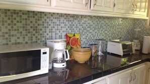 A kitchen with white cabinets, a black countertop, a microwave, a toaster, a blender, and a fruit-themed book. - BK Villas (Maxwell)