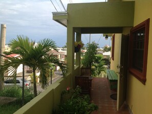 Un balcón con vista a una zona residencial, un banco de madera y plantas en macetas.