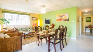 A living room with a sofa, chairs, a dining table set for four, and a television on the wall. - BK Villas (Maxwell)