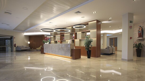 Un moderno vestíbulo de hotel con un mostrador de recepción de mármol, lámparas circulares y una gran planta en maceta.