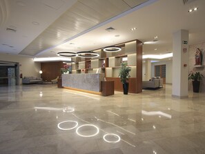 A modern hotel lobby with a marble reception desk, circular light fixtures, and a large potted plant. - Consolata Hotel (Ourem)