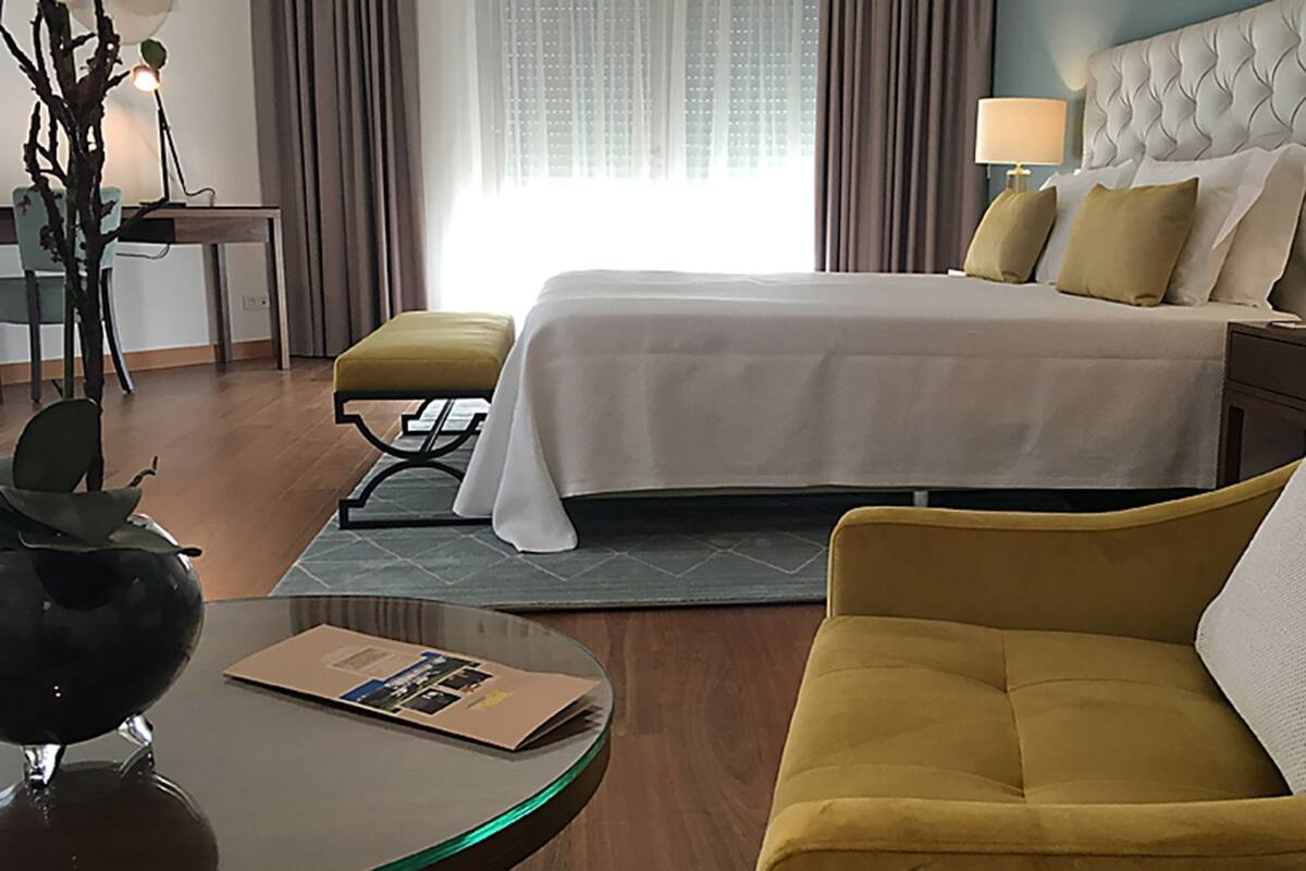A hotel room with a bed, a sofa, a table, and a lamp.