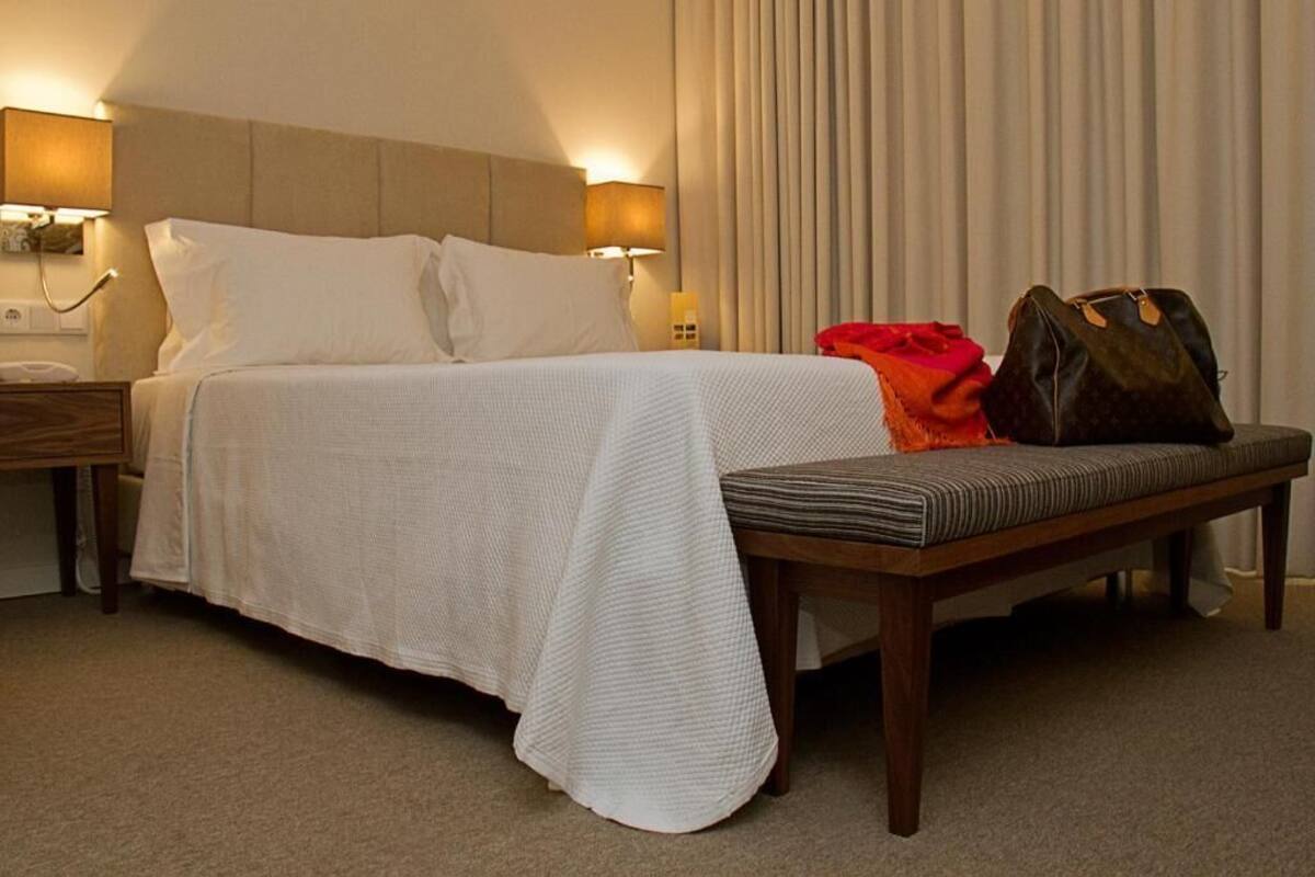 A hotel room with a bed, bedside tables, a bench, and a curtain.