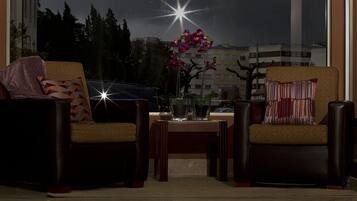 Una habitación con dos sillones, una mesita con un jarrón de flores y un ventanal con vistas a edificios y árboles.