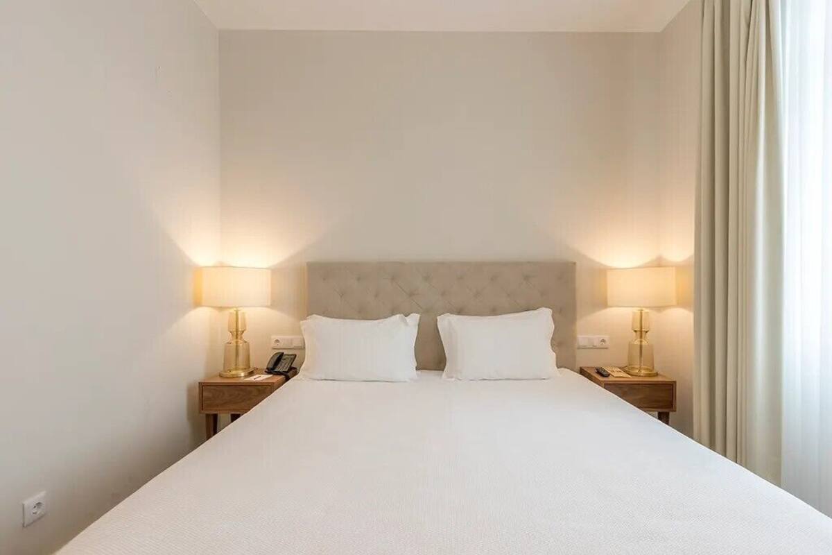A hotel room with a large bed, two bedside tables with lamps, and a neutral-colored headboard.