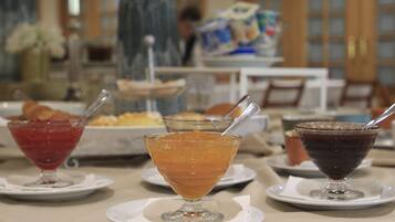 Ein Tisch mit drei Dessertgläsern, die verschiedene Getränke enthalten, eine Vase mit Blumen und ein Speisebereich im Hintergrund.