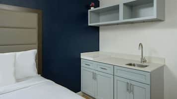 A bedroom with a bed, a nightstand, a small white sink, and a cabinet.