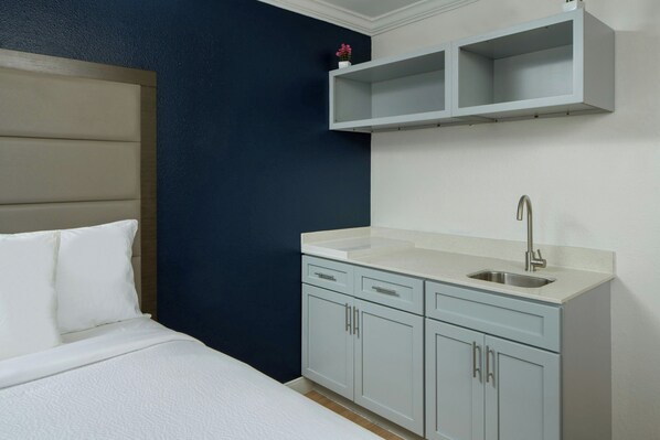 A bedroom with a bed, a nightstand, a small white sink, and a cabinet.