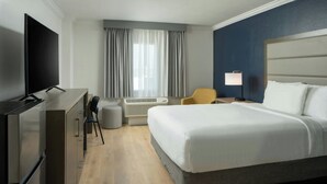 A hotel room with a large bed, a desk with a flat-screen TV, a chair, a lamp, and an air conditioning unit. - City Express by Marriott New Orleans 1-10 (New Orleans)