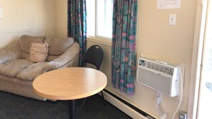 A room with a beige sofa, a round wooden table, and a wall-mounted air conditioner. - Bluebird Motel (Innisfail)