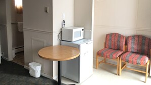 A small, compact room with a round table, a microwave, a refrigerator, and a patterned sofa. - Bluebird Motel (Innisfail)