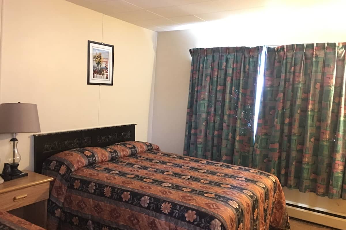 Une chambre avec un lit, une table de chevet, une lampe et une fenêtre avec des rideaux.