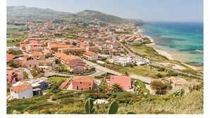 Un pueblo costero con edificios a lo largo de la playa, una vista despejada del mar y un paisaje montañoso de fondo.