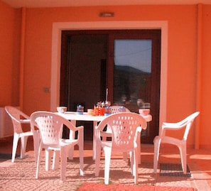 Un espace extérieur aménagé pour les repas, avec une table et quatre chaises en plastique blanc.