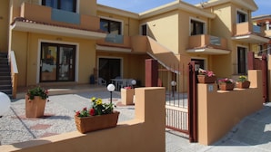 Un edificio residencial de varios pisos con balcones, un acceso con portón y mobiliario exterior.