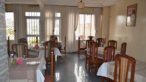 A dining area with multiple tables and chairs, large windows with curtains, and a tiled floor. - Felydac Hotel (Yaoundé)