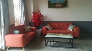 A living room with two red sofas, a coffee table, and a large painting on the wall. - Felydac Hotel (Yaoundé)