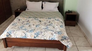 A bedroom with a bed, a nightstand, a wall-mounted light fixture, and a tiled floor. - Felydac Hotel (Yaoundé)