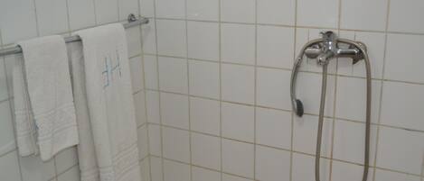 A bathroom with white tiled walls, a shower with a handheld showerhead, and two white towels hanging on a rack.