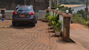 A car parked on a paved driveway with a white fence and potted plants along the side. - Felydac Hotel (Yaoundé)