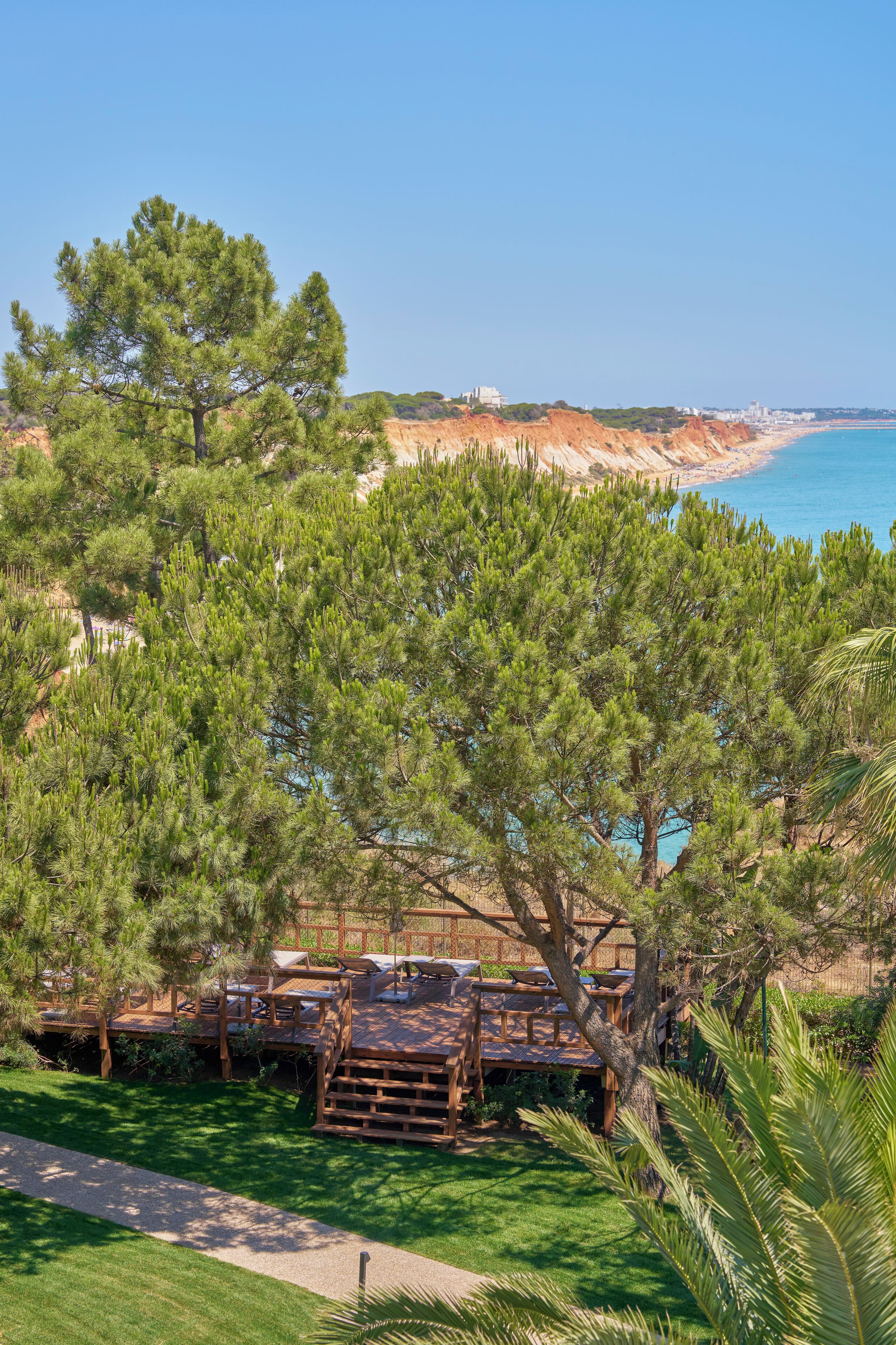 Une terrasse en bois avec des sièges extérieurs, entourée d’une végétation luxuriante et offrant une vue sur la plage.