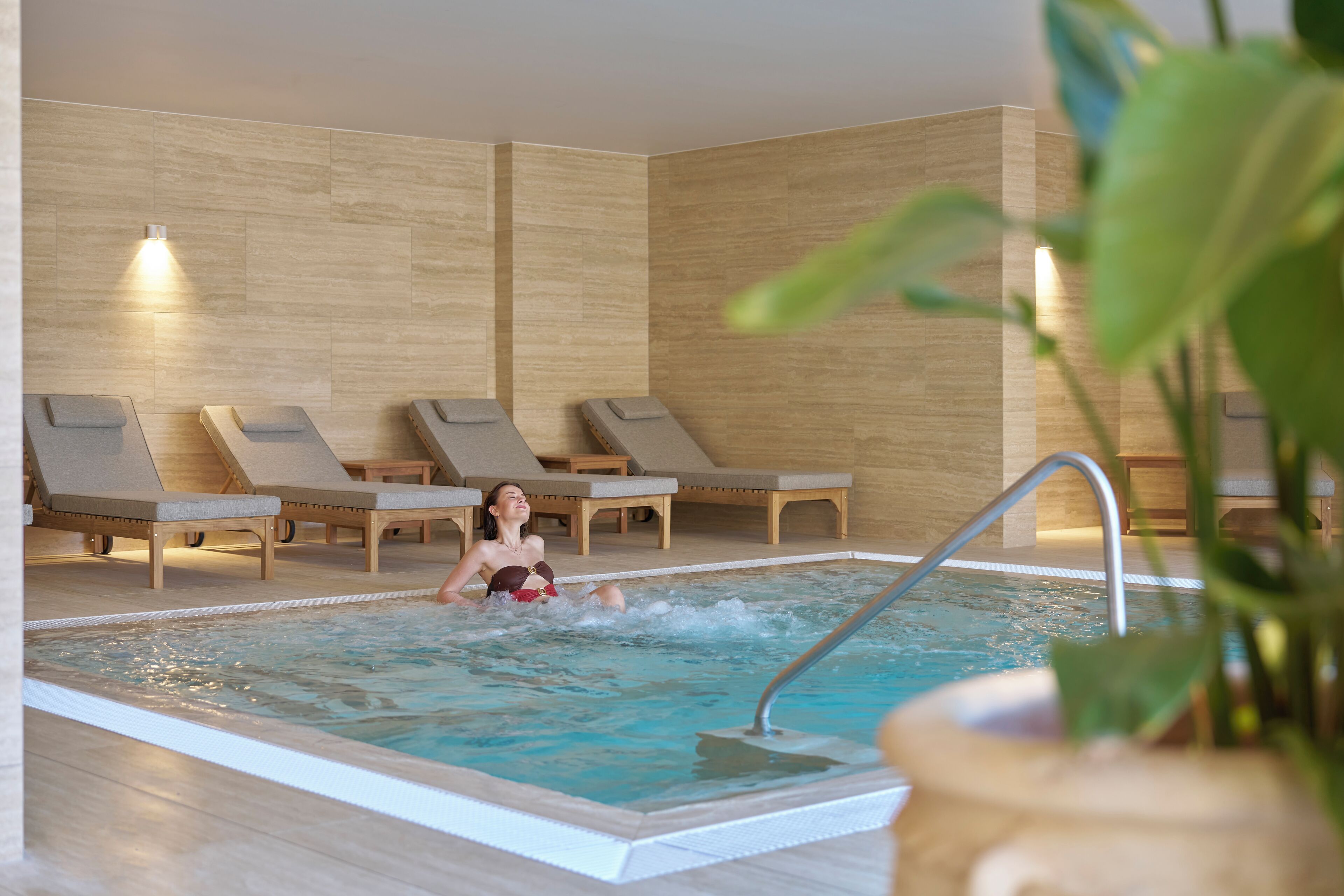 Area piscina con idromassaggio, poltrone relax e una persona a bordo.