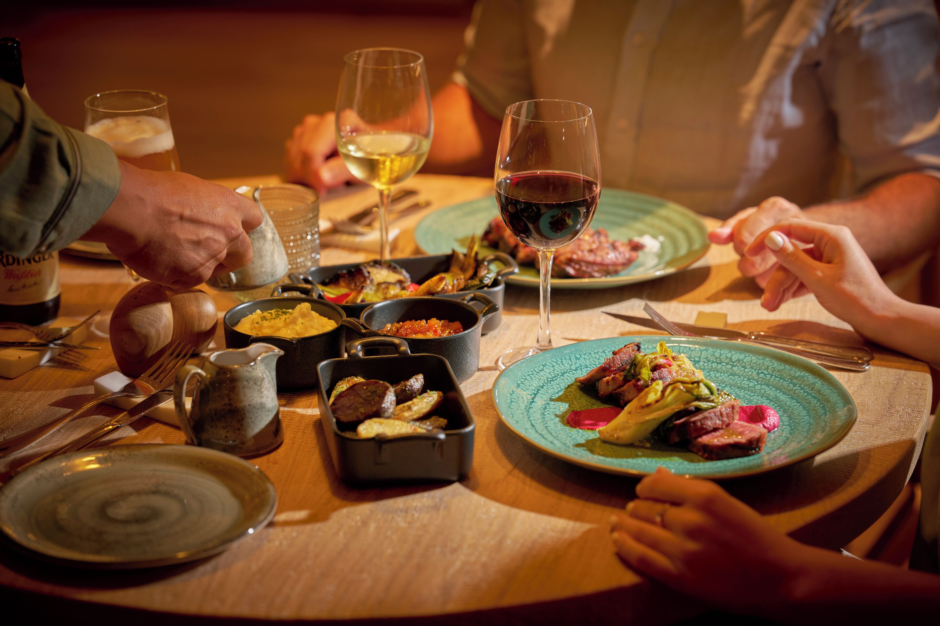 A dining table with plates of food, wine glasses, and a bottle of wine.