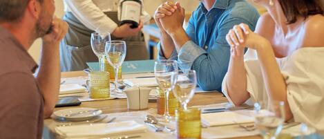 A dining table set for four people with a waiter holding a bottle of champagne.