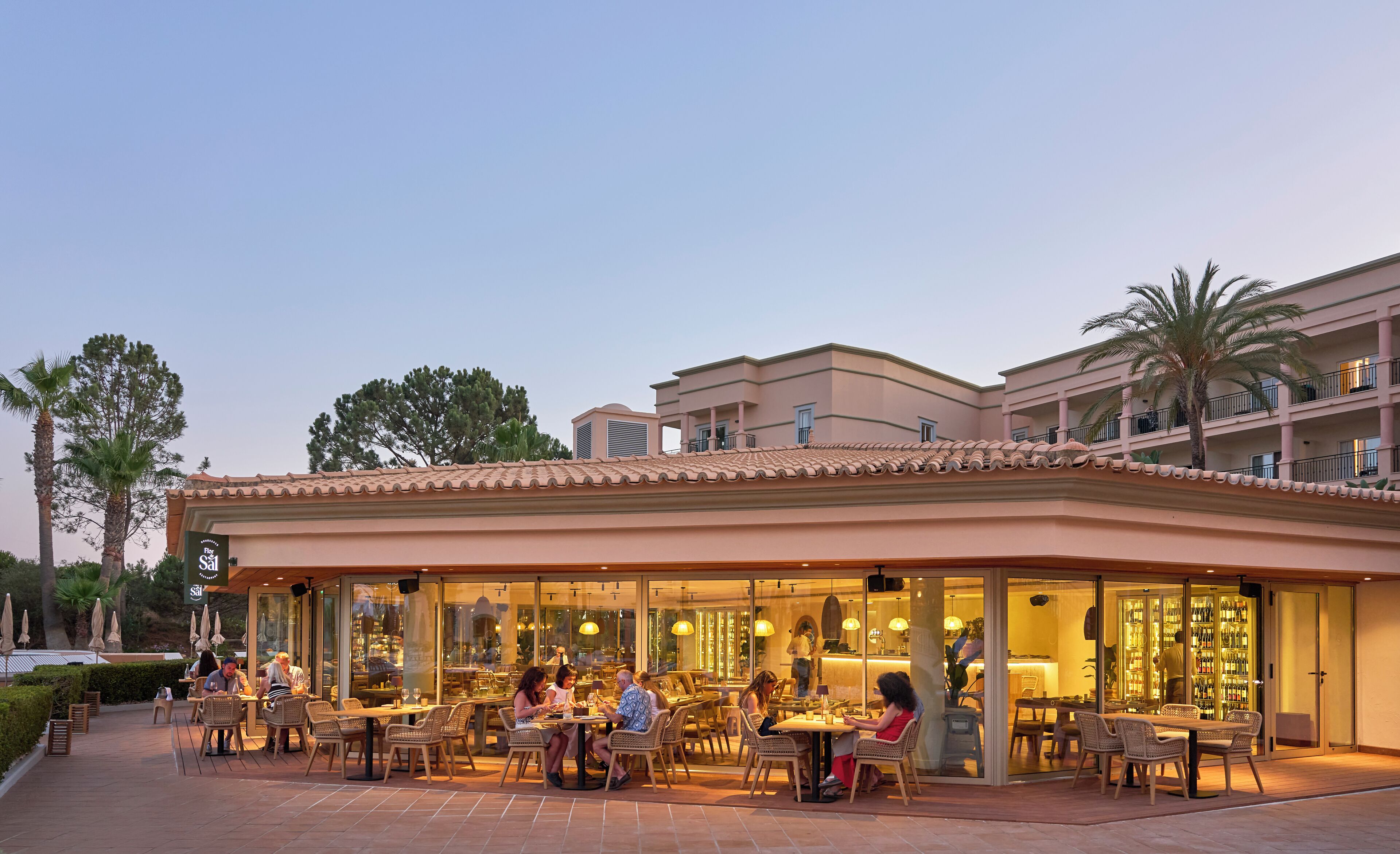 Een restaurant met terras, een glazen gevel en uitzicht op een meerhoog gebouw met balkons.