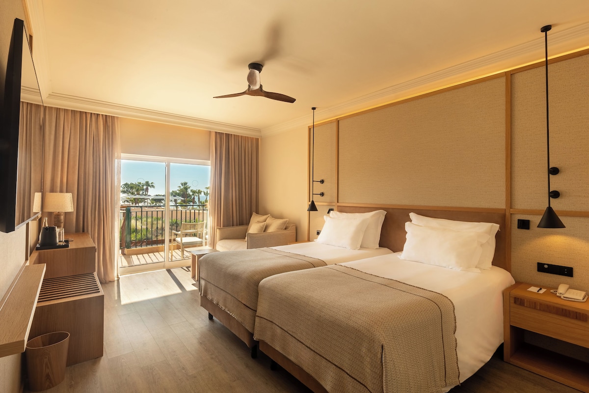 Habitación de hotel con dos camas, un balcón, televisión, escritorio y teléfono.