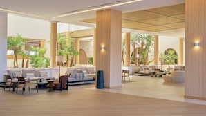 Un vestíbulo amplio con varias zonas de estar, grandes columnas de madera y plantas de interior.