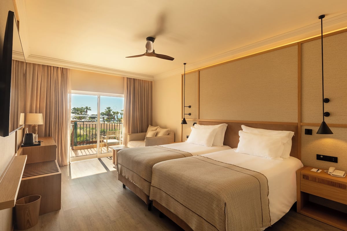 A hotel room with two beds, a balcony, a TV, a desk, and a phone.
