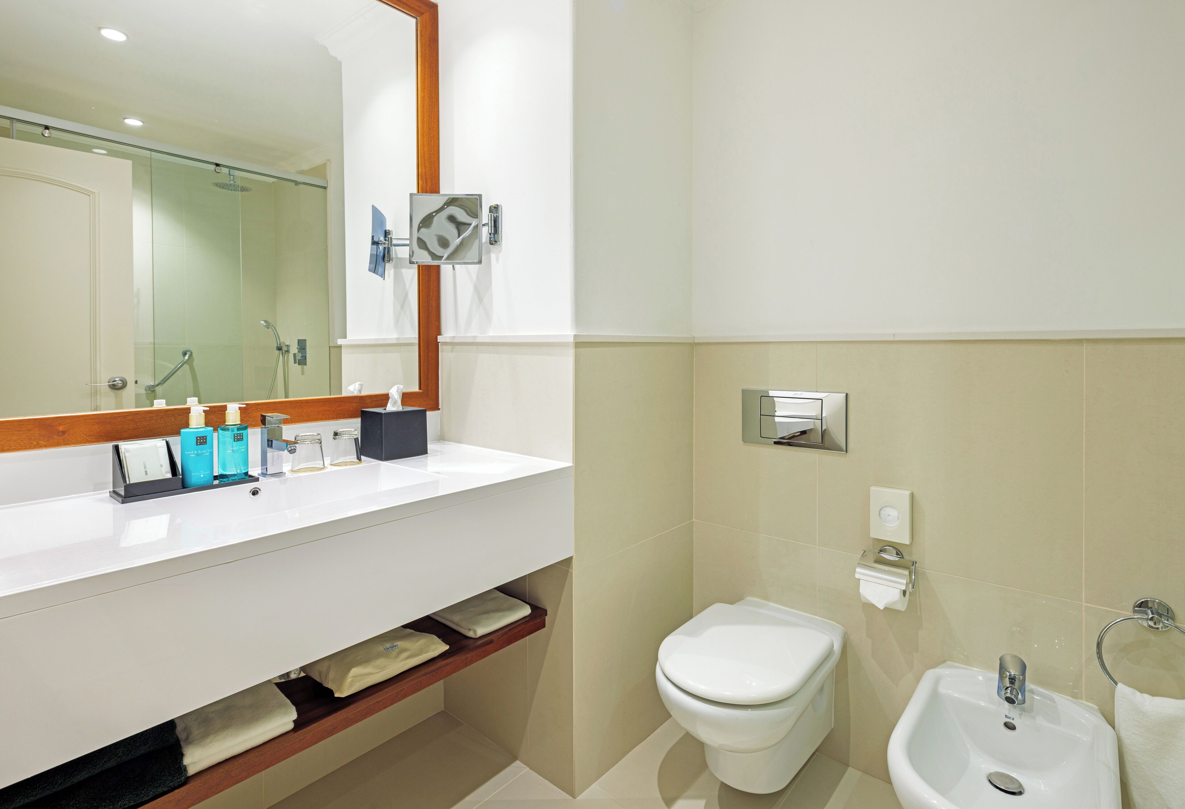 A modern bathroom with a white sink, a glass-enclosed shower, a white toilet, and a bidet.