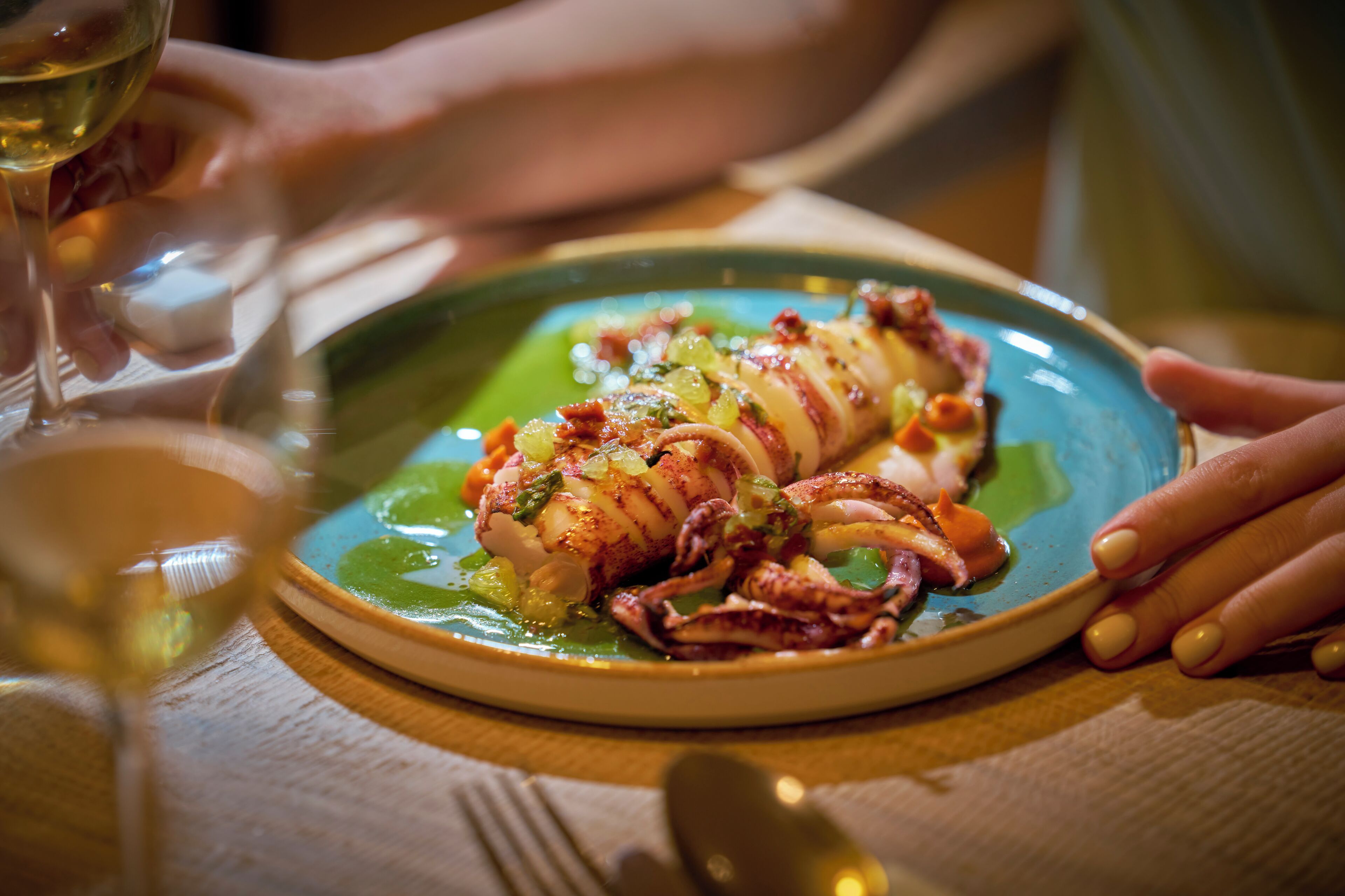 Une assiette de nourriture contenant un plat de fruits de mer, un verre de vin blanc et la main d’une personne tenant l’assiette.