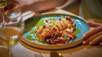 Une assiette de nourriture contenant un plat de fruits de mer, un verre de vin blanc et la main d’une personne tenant l’assiette.