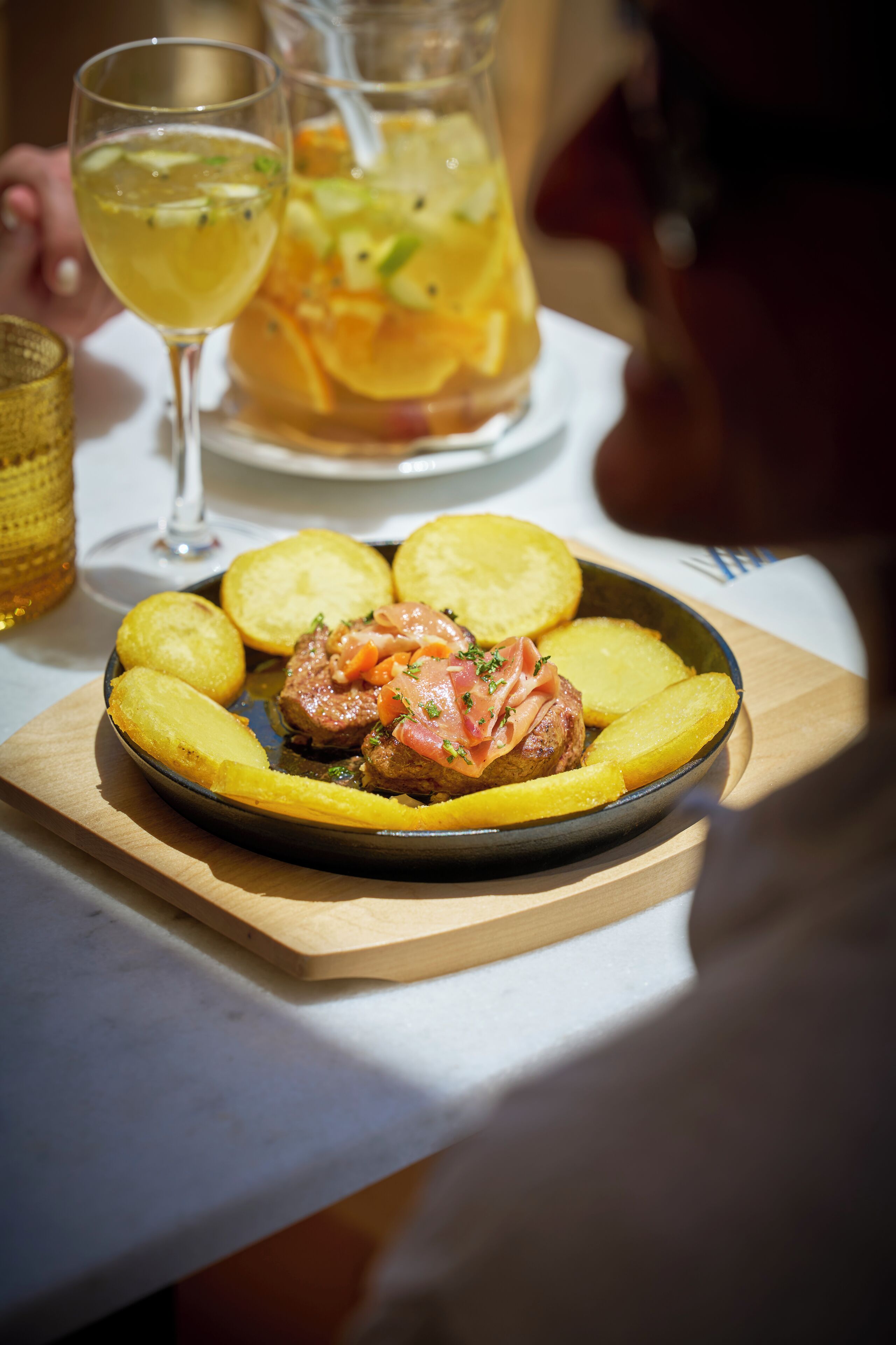 A plate of food with potatoes and a meat dish, accompanied by a glass of wine and a pitcher of fruit drink.