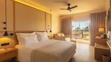 Habitación de hotel con una cama grande, un escritorio con lámpara, ventilador de techo y vistas al exterior.